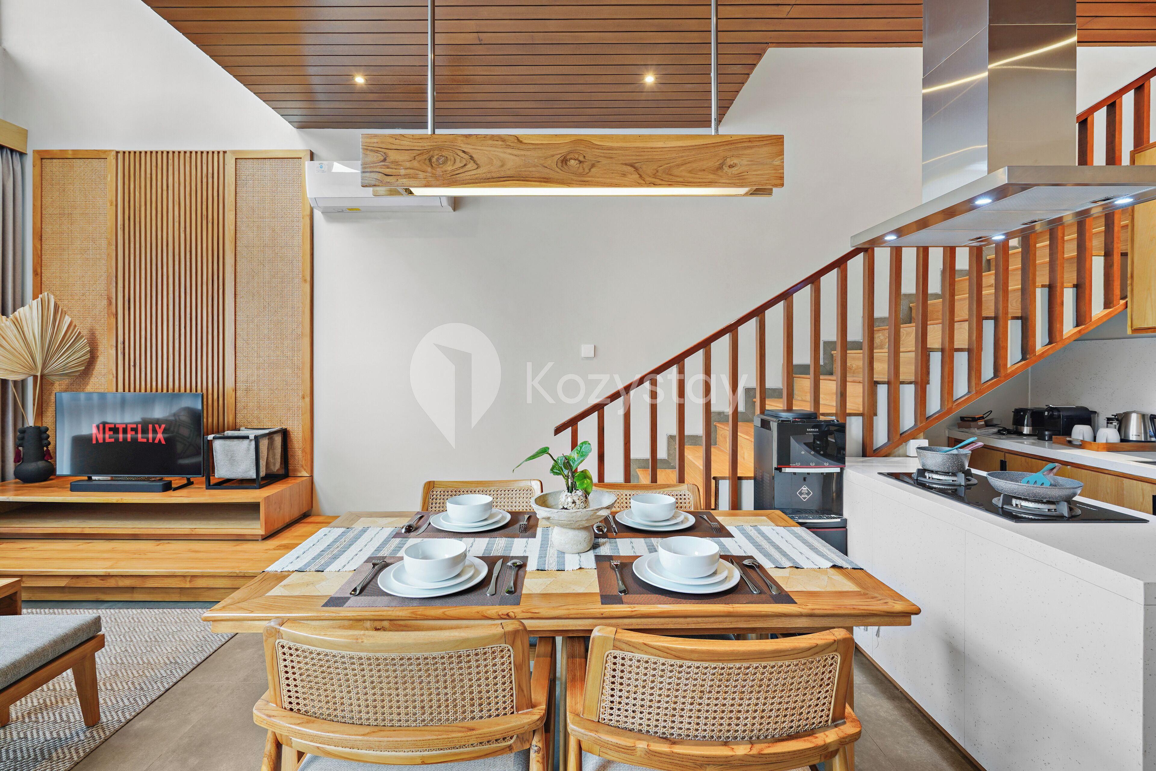 Un salon moderne comprenant un coin repas, des meubles en bois, un escalier et un espace cuisine.