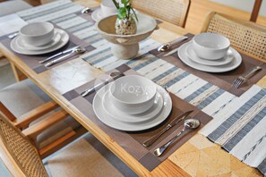 A dining table set with white plates, bowls, and silverware, arranged on a striped placemat. - Sundari Villa by Kozystay - Canggu (Canggu)