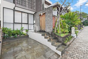 A modern house with a stone facade, a wooden door, and a small garden with tropical plants. - Sundari Villa by Kozystay - Canggu (Canggu)