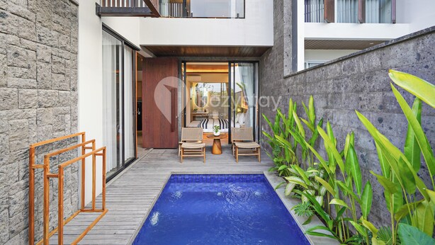 A modern outdoor pool area with a wooden deck, two wicker chairs, and a small table.