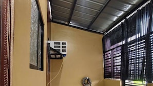 A room with a tiled floor, a black table with a plant, a wall-mounted air conditioner, and a window with blinds. - Cozy House for Rent in Dadiangas, General Santos City (General Santos)