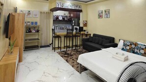 A compact hotel room with a bed, a desk, a chair, a sofa, a fan, and a kitchenette in the background. - Cozy House for Rent in Dadiangas, General Santos City (General Santos)