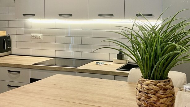 Una cocina moderna con armarios blancos, una placa de inducción negra y una maceta tejida en la encimera.