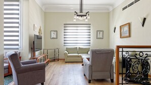 A living room with two armchairs, a sofa, a TV, and a large window with blinds.