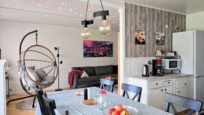 A modern kitchen with a white refrigerator, a microwave, and a coffee maker on the countertop. There is a dining table with chairs and a hanging chair in the living area.