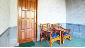 A wooden door with a decorative panel, two wicker chairs with blue cushions, and a stone wall with a herringbone pattern. - Belvilla Bogor near Citra Alam Riverside formerly Jatimas Hijau (Cisarua)