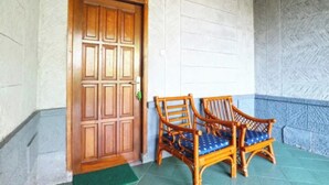 A wooden door with a decorative panel, two wicker chairs with blue cushions, and a stone wall with a herringbone pattern. - Belvilla Bogor near Citra Alam Riverside formerly Jatimas Hijau (Cisarua)