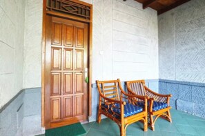 A wooden door with a decorative panel, two wicker chairs with blue cushions, and a stone wall with a herringbone pattern. - Belvilla Bogor near Citra Alam Riverside formerly Jatimas Hijau (Cisarua)