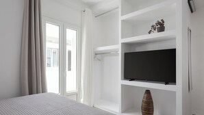 A modern bedroom with a bed, a TV on a white shelf, and a potted plant. - Deluxe Suite, Palma Elegant Suites (Paros)