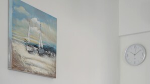 A white dining table with two chairs, a painting of sailboats on the wall, and a clock. - Deluxe Suite, Palma Elegant Suites (Paros)