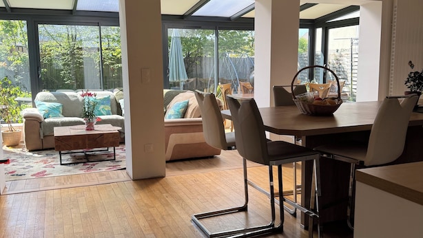 Amplia sala de estar con suelo de madera, una mesa de comedor con sillas, un sofá y un amplio ventanal corredero que da a un jardín.