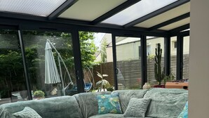 Una sala moderna con un sofá seccional, una mesa de centro de madera y vistas al jardín a través de amplios ventanales.