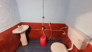 A small, compact bathroom with a white toilet, a white sink, and a red bucket.