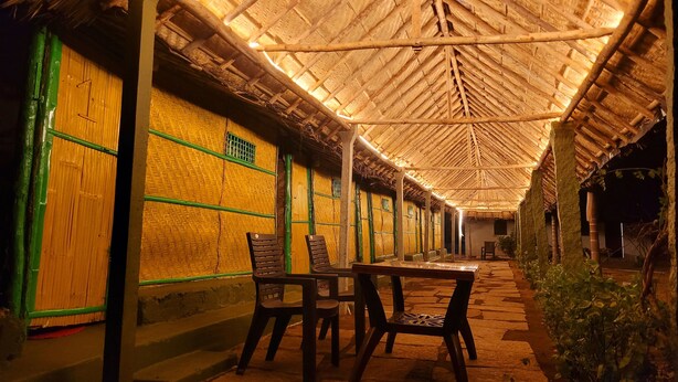 A covered outdoor seating area with a thatched roof, wooden walls, and a paved walkway.