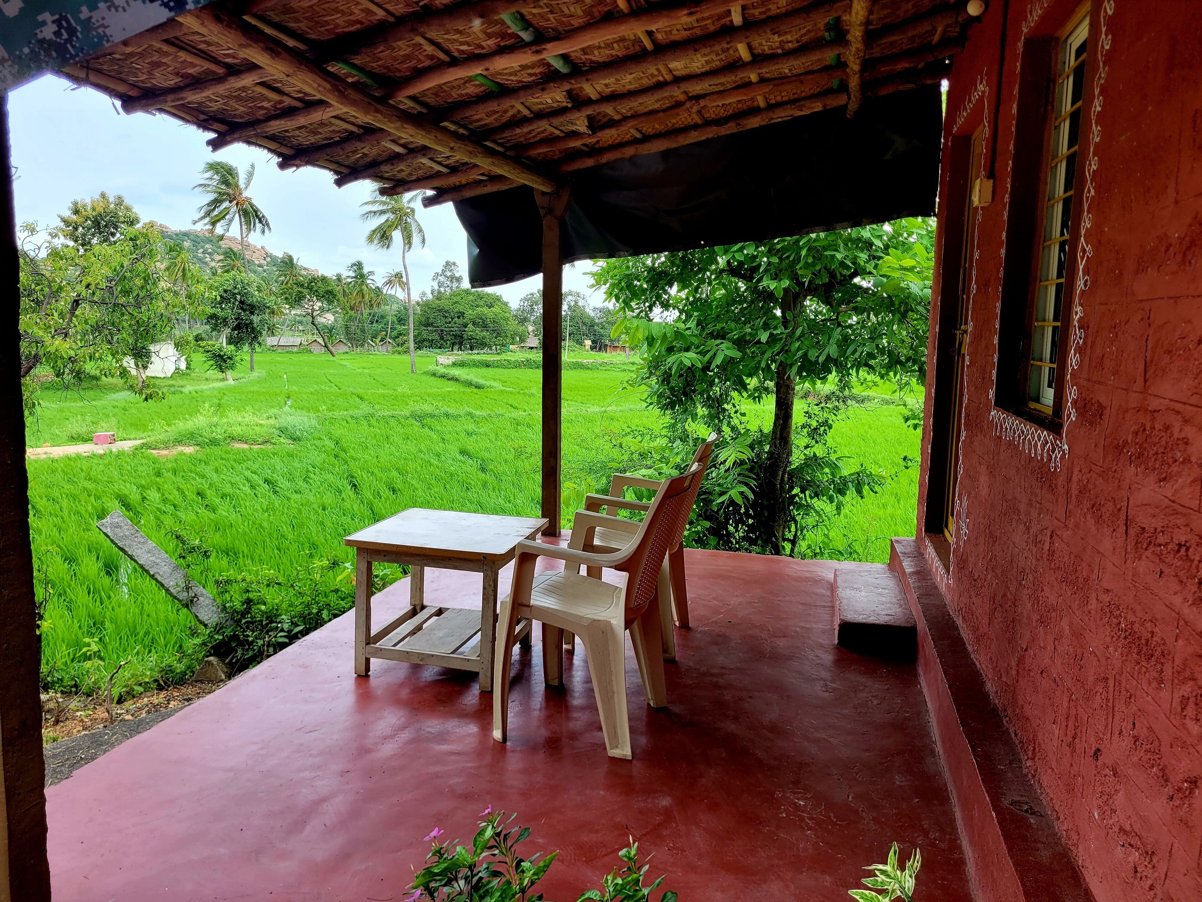 A covered outdoor area with a table and chairs, overlooking a lush green field.