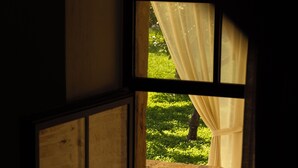 Vista a través de una ventana con un banco y un candelabro, una pequeña mesa con una vela y una planta en maceta.