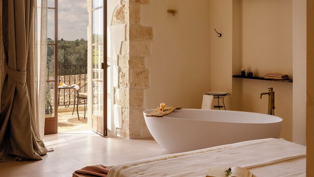 Un dormitorio con una cama grande, una bañera y vistas a través de una puerta abierta.
