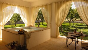 Un cuarto de spa con un jacuzzi, una mesa con un florero y vistas a un jardín.