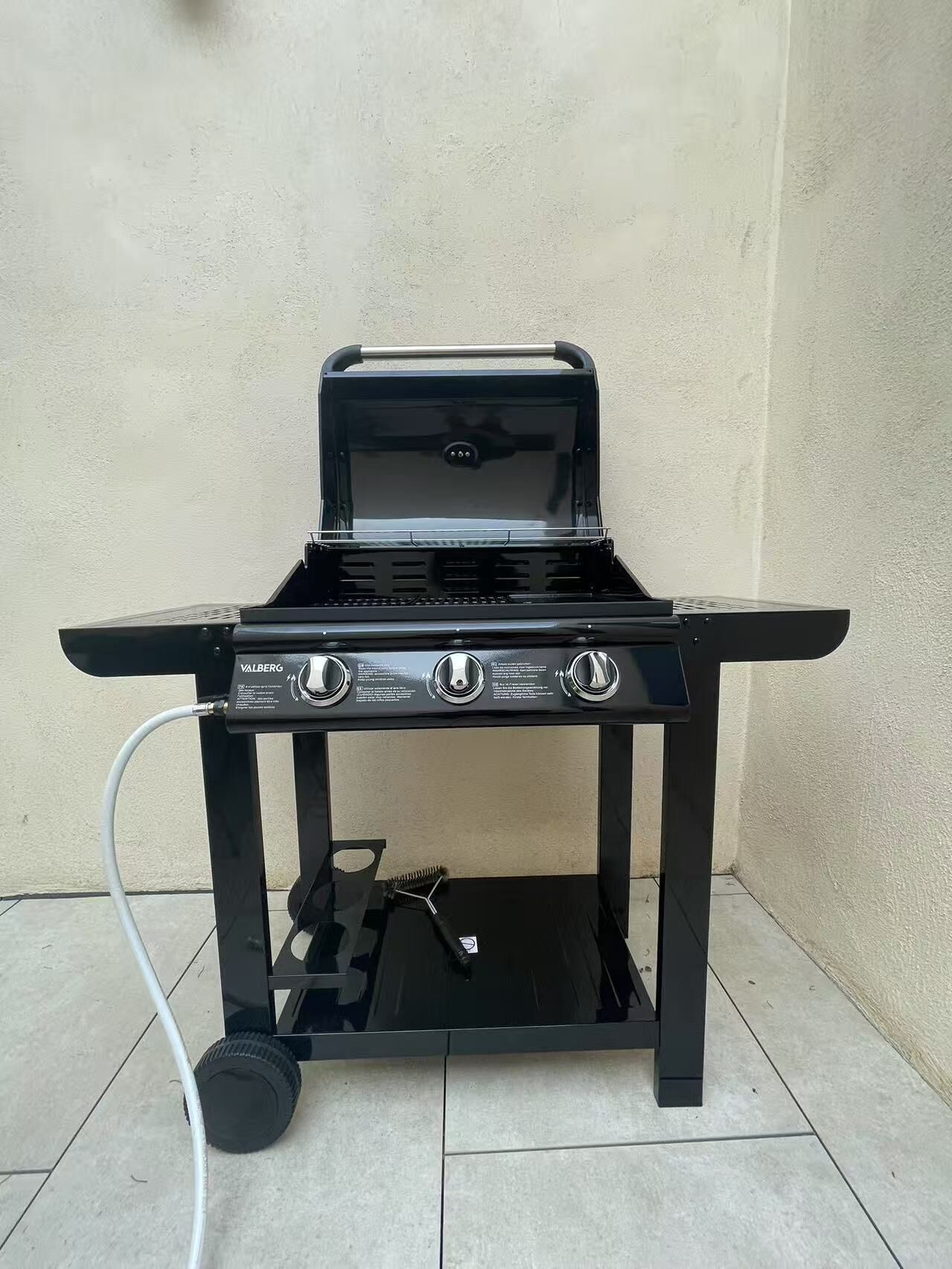 Een zwarte buitenbarbecue met vier branders en een extra brander aan de zijkant, een bedieningspaneel en een slang.