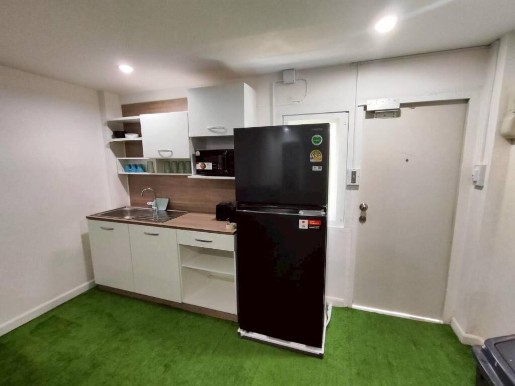 Une cuisine de taille réduite avec un réfrigérateur noir, des placards blancs et un tapis vert.