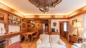 Un salon chaleureux, décoré de meubles en bois, avec une cheminée, un canapé, une table à manger et un lustre.