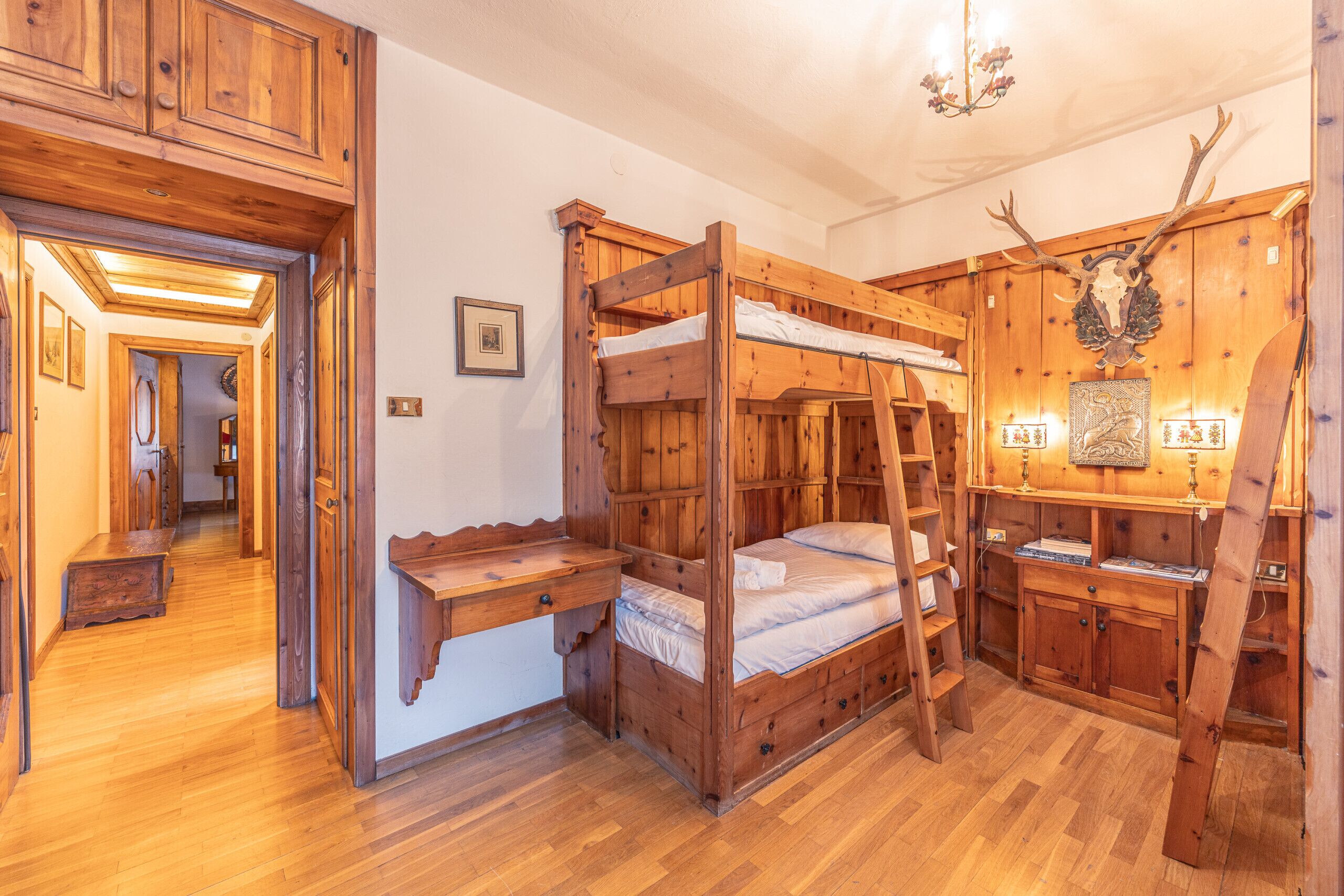 A rustic wooden room with bunk beds, a desk, and a ladder.