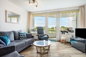 A modern living room with a sofa, a round coffee table, a chair, a TV, and a balcony with a view.