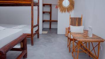 Una habitación con literas, una mesa de madera con sillas, un espejo y un estante pequeño.