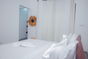 Habitación de hotel con cama, cabecera de madera, espejo tipo sol en la pared y puerta que conduce a otra habitación.