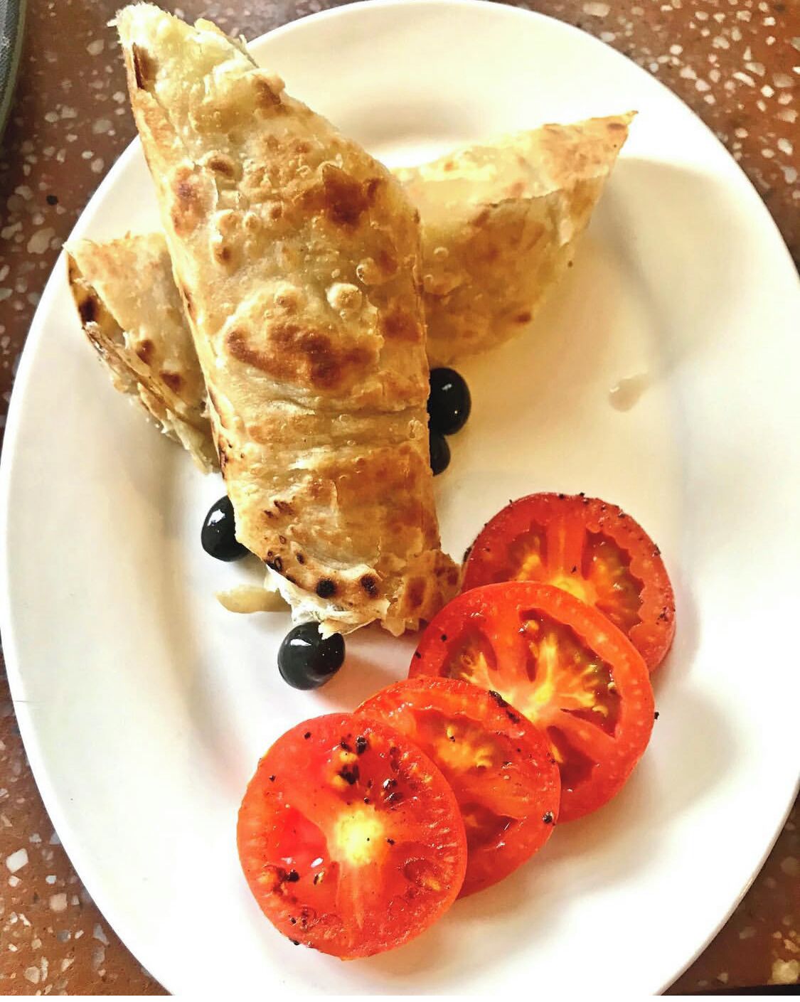 A plate with two folded items, possibly pastries, and sliced tomatoes.