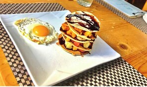 Une assiette avec un œuf au plat et une pile de crêpes nappées de sirop.