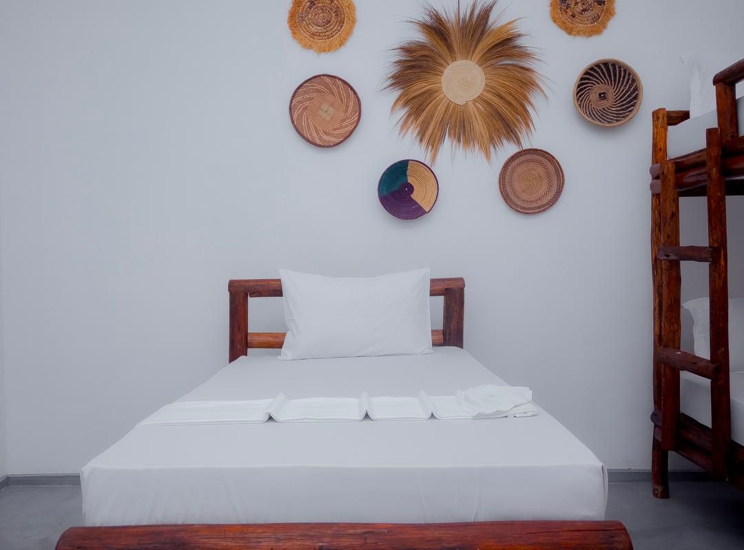 A neatly made bed with white linens and a wooden headboard in a room with a plain white wall.