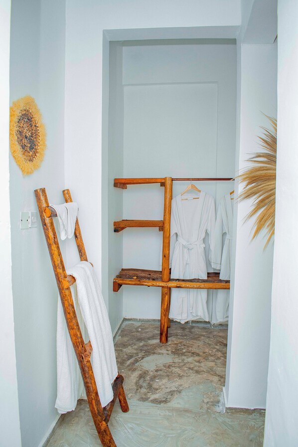 Une salle de bain avec un porte-serviettes en bois où sont rangées des serviettes et un peignoir, une porte blanche et une plante.