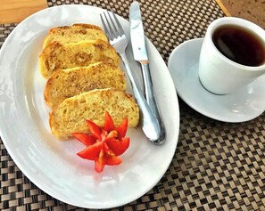 Une assiette blanche avec des tranches de pain grillé, une garniture de tomates et une tasse de café, le tout posé sur une nappe à motifs tissés.