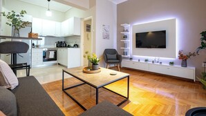 Ein modernes Wohnzimmer mit Holzboden, einer Couch, einem Couchtisch und einem an der Wand befestigten Fernseher.