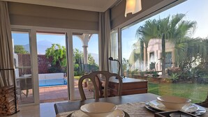 A dining area with a view of a swimming pool and garden. - Villa Gecko (La Puntilla)