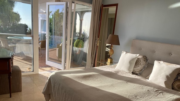 A bedroom with a large bed, a nightstand, a lamp, and a view of the outdoors through a sliding door. - Villa Gecko (La Puntilla)