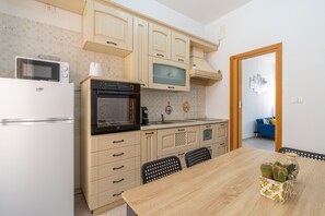 Cocina compacta con microondas, horno y pileta, muebles de madera y comedor con mesa y sillas.