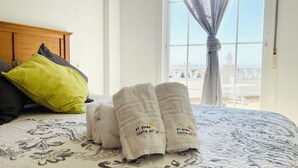 A bed with a floral-patterned bedspread, a wooden headboard, and a view of the sea through a window with sheer curtains. - White House with Sea Views by At Home Costa del Sol (Torrox Costa)