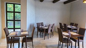 A dining area with multiple tables and chairs, large windows with a view of greenery, and a ceiling with exposed beams. - Ere's Palace (Tbilisi)