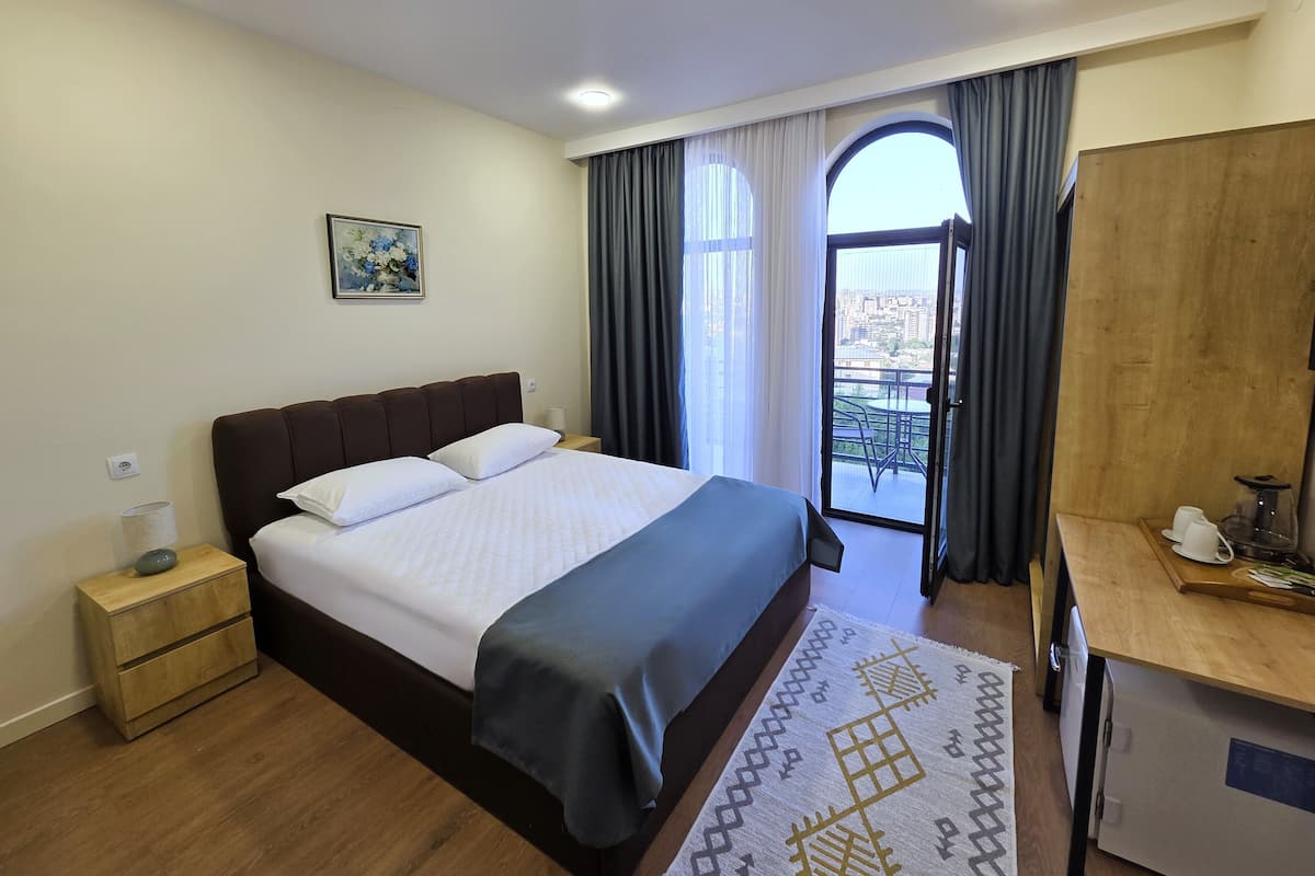 A hotel room with a bed, bedside table, and a view of the city through a large window.