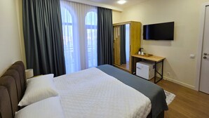 A hotel room with a bed, a desk with a TV, a small fridge, and a wardrobe. - Ere's Palace (Tbilisi)