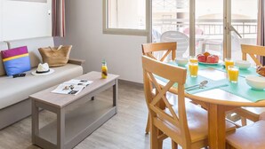 A modern living room with a sofa, a coffee table, and a dining area with chairs and a table set for breakfast. - BLUE AIR-CONDITIONED STUDIO CABIN SLEEPS 4 (Sainte-Maxime)