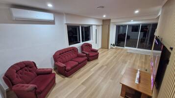 A living room with a sofa set, a flat-screen TV, and a sliding glass door leading to a balcony.