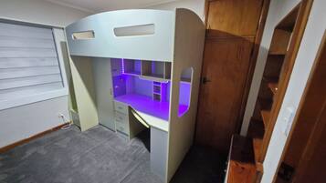 A bunk bed with a desk underneath, a small ladder, and a wooden wardrobe to the right.
