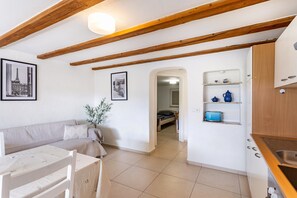 Una habitación con sofá, una mesa de comedor, una zona de cocina con estantes, y una puerta que da a otra habitación.