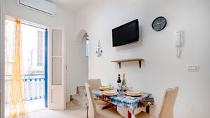 Un comedor con una mesa dispuesta para cuatro personas, un televisor montado, un reloj y un teléfono en la pared.