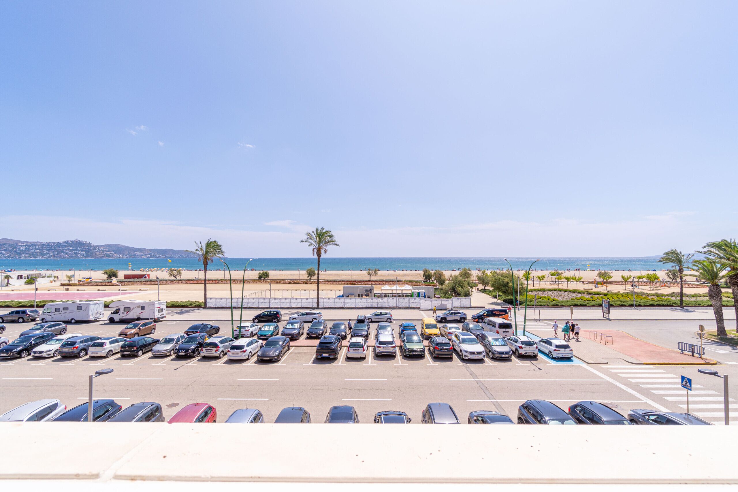 Ein Parkplatz mit mehreren Autos und Blick auf den Strand im Hintergrund.