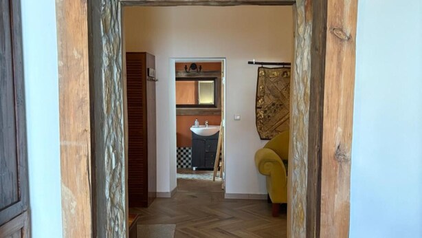 A hallway with a herringbone floor leading to a bathroom with a sink and mirror.