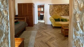 A room with a bed, a yellow sofa, a wooden wardrobe, and a herringbone-patterned floor.